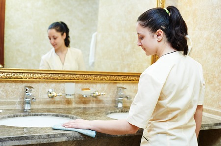 Hotel service. female housekeeping worker cleaning table from dust in bathroomの写真素材