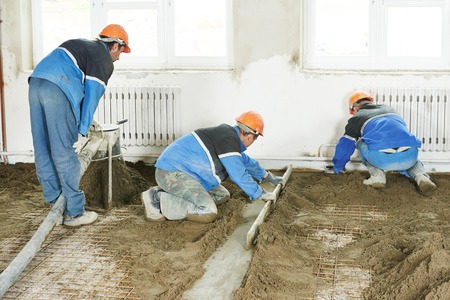 Plasterer workers at indoor concrete cement floor topping with floatの写真素材