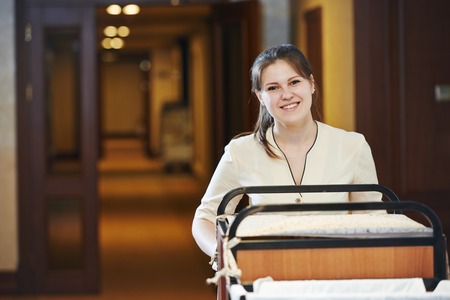 Hotel room service. female housekeeping worker with bedclothes linen in cart
