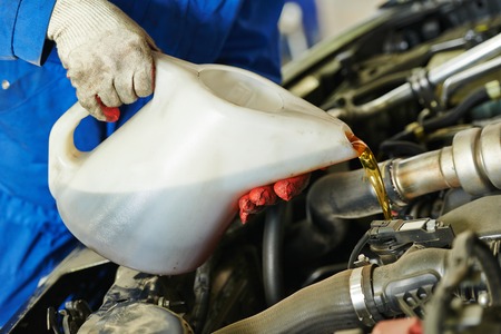 auto mechanic technician replacing and pouring motor oil into automobile engine at maintenance repair service stationの写真素材