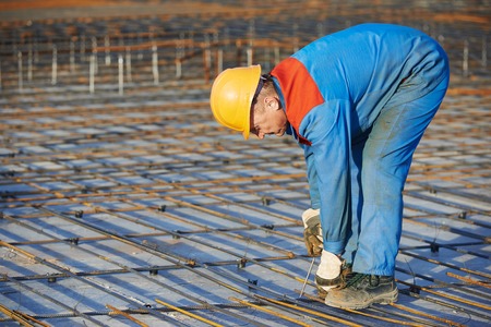 builder worker knitting metal rebars into framework reinforcement for concrete pouring at...