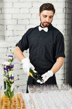 Waiter bartender pouring white wine into glasses at party eventの写真素材