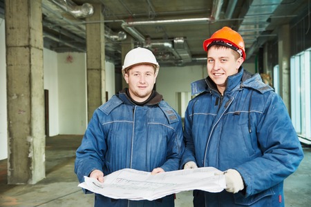 young male engeneers workers foreman at a indoors building site with blueprintsの写真素材
