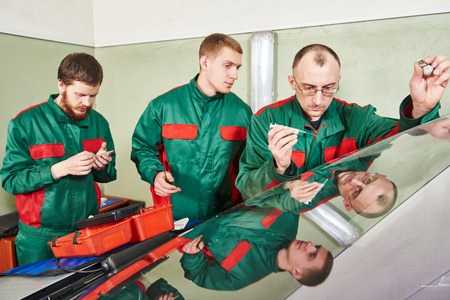 Automobile glazier repairman at windscreen repair of a car in auto service station garage