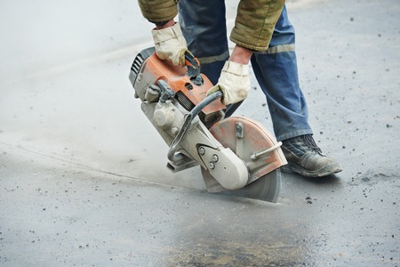 Builder worker with cut-off machine power tool breaking asphalt at road construction siteの写真素材