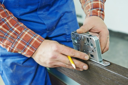 Close-up carpenter hands with doorlock during lock process installation into wood doorの写真素材