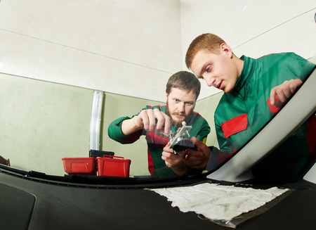 Automobile glazier repairman teaching or discussing with partner windscreen repair of a car in auto...