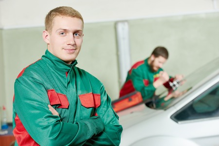 Automobile glazier repairman portrait in front of worker repairing car windscreen in auto service station garageの写真素材