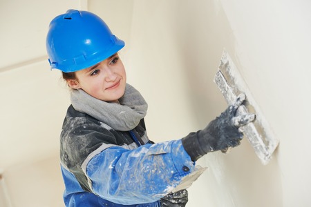 female plasterer painter at indoor wall renovation decoration stopping with spatula and plasterの写真素材
