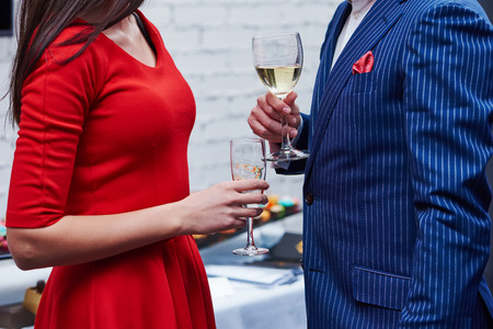 Two guests of formal evening party celebration holding glasses of wine in their hands