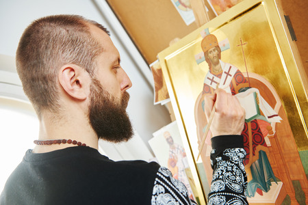 Religious icon painter man paints a new icon with brush at workshop