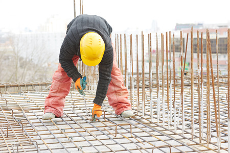 construction worker making reinforcement with metal rebar rods at building site