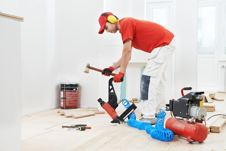 carpenter worker installing wood floor parquet board during flooring work with hammerの写真素材