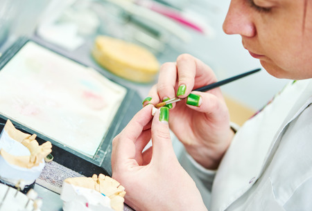 Dental technician painting tooth during work on dentures at prosthesis laboratoryの写真素材