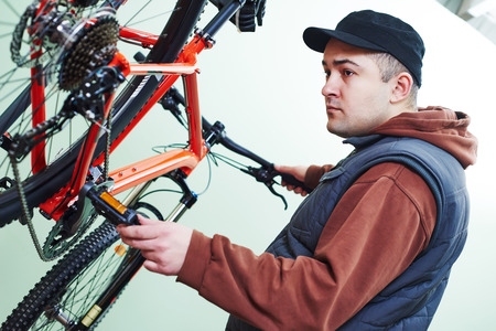 Bike maintenance: mechanic serviceman repairman installing assembling or adjusting bicycle gear on wheel in workshopの写真素材