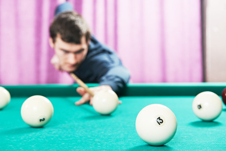 Young player man with cue playing billiard or snooker game