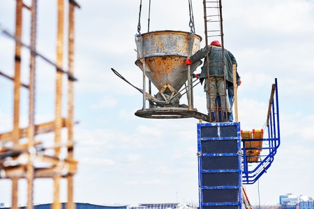 concreting work: construction site workers pouring concrete into formwork at building area with skipの写真素材