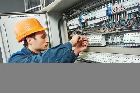 electrician with screwdriver tighten up switching electric actuator equipment in fuse box