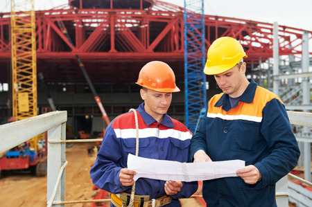 Two engineer builders with blueprint plan at construction site