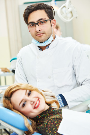 Portrait of male asian dentist wearing lab coat while sitting in clinic with clientの写真素材