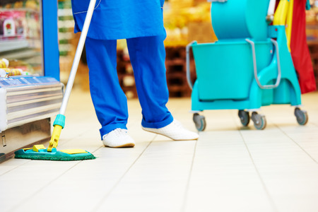 Female cleaner worker in uniform  with mop cleaning the floor of supermarket shop storeの写真素材