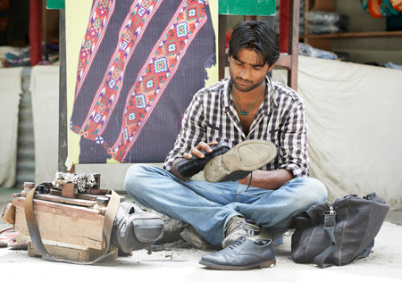young shoeblack man cleaning boots on street in indiaの写真素材