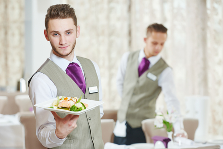 Waiter occupation. Young man with food on dishes servicing in restaurant