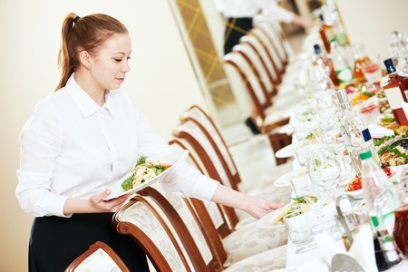 Restaurant catering services. Waitress with salad dish serving banquet tableの写真素材