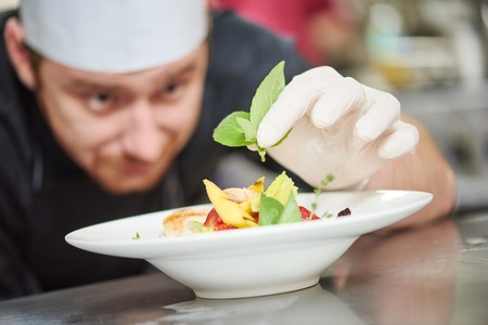 male cook chef decorating garnishing prepared salad dish on the plate in restaurant commercial kitchenの写真素材