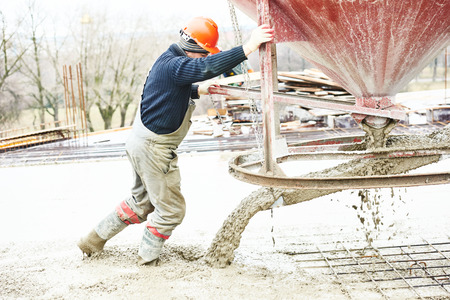 Concreting work. Construction site worker during concrete pouring into formwork at building area with barrel skipの写真素材