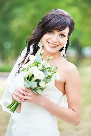 Wedding theme. Happy cheerful beautiful bride with fresh flower bouquet outdoors in a park.の写真素材