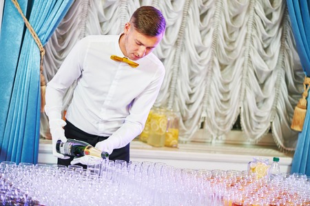 Waiter bartender pouring red wine into glasses at party eventの写真素材