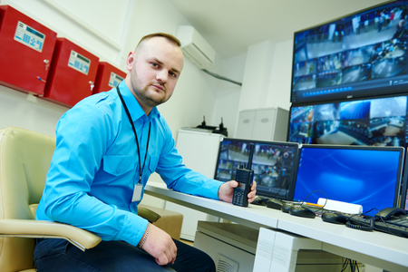 security guard officer portrait with portable radio transmitter in front of video monitoring...