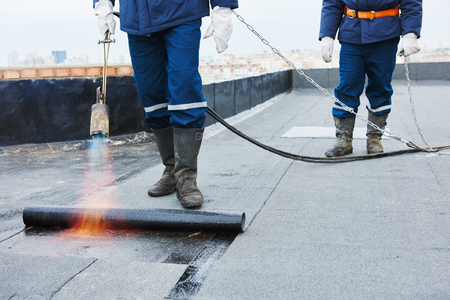 Flat roof installation. Heating and melting bitumen roofing felt by flame torch at construction siteの写真素材