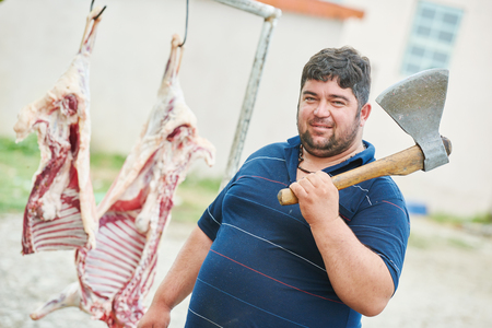 Real authentic male butcher with axe and sheep carcass meat outdoorsの写真素材