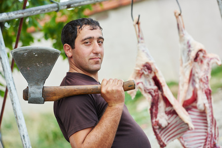 Real authentic male butcher with axe and sheep carcass meat outdoorsの写真素材