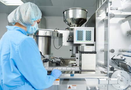 Pharmaceutics. Pharmaceutical industry worker operates blister and cartoning packaging machine at...