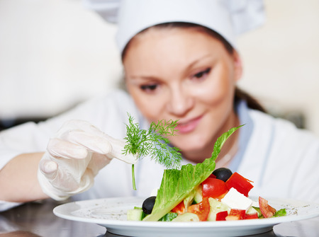 female cook chef decorating garnishing prepared salad food dish on the plate in restaurant commercial kitchenの写真素材