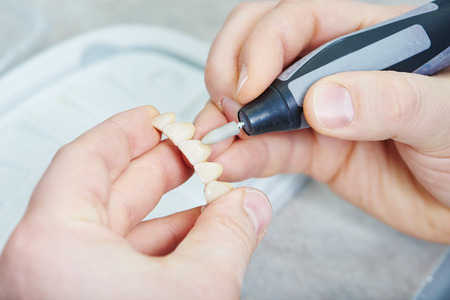 Dental technician finishing tooth during work on dentures at prosthesis laboratory