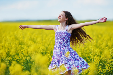 young happy girl in colorful dress with flower garland at yellow green rape seed meadow expressing joyの写真素材