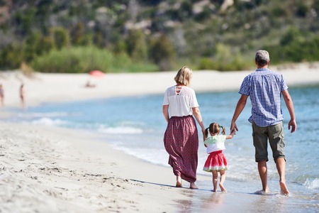 young family walking with little girl child on sea beachの写真素材