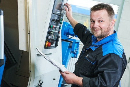 Industrial factory worker or service engineer operating cnc turning lather machine at factory in...