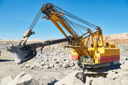 Heavy excavator extracting granite rock or iron ore at opencast mining quarry