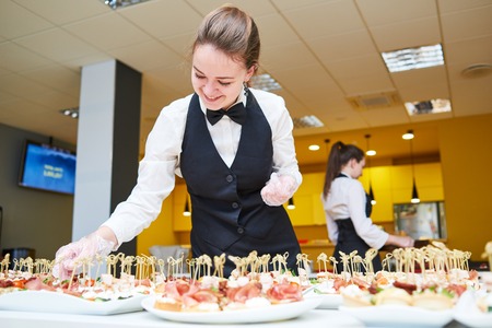 Restaurant service or waiter occupation. Female waitress worker serving table with food plates at catering in cafeの写真素材