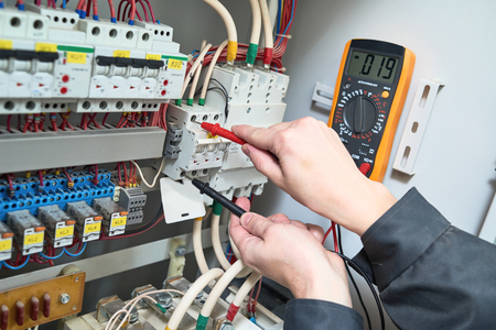 Electrician works. male technician examining fusebox with digital multimeter ac dc testerの写真素材