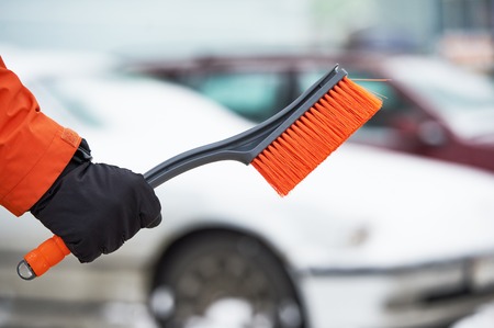 car cleaning from snow in winter. Hand with brush in front of snowy automobile.