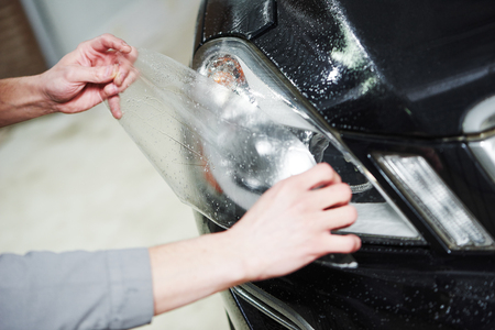 Hands of repairman mechanic with protective film while covering and protecting automobile headlight lampの写真素材