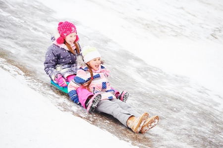 Children girls having fun in winter riding ice slide