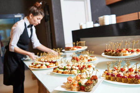 Restaurant service or waiter occupation. Female waitress worker serving table with food plates at catering in cafeの写真素材