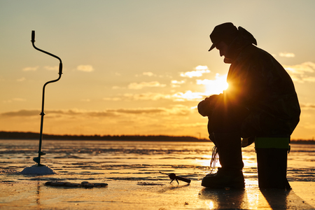 The angler fisherman at ice winter fishing. Sunsetの写真素材
